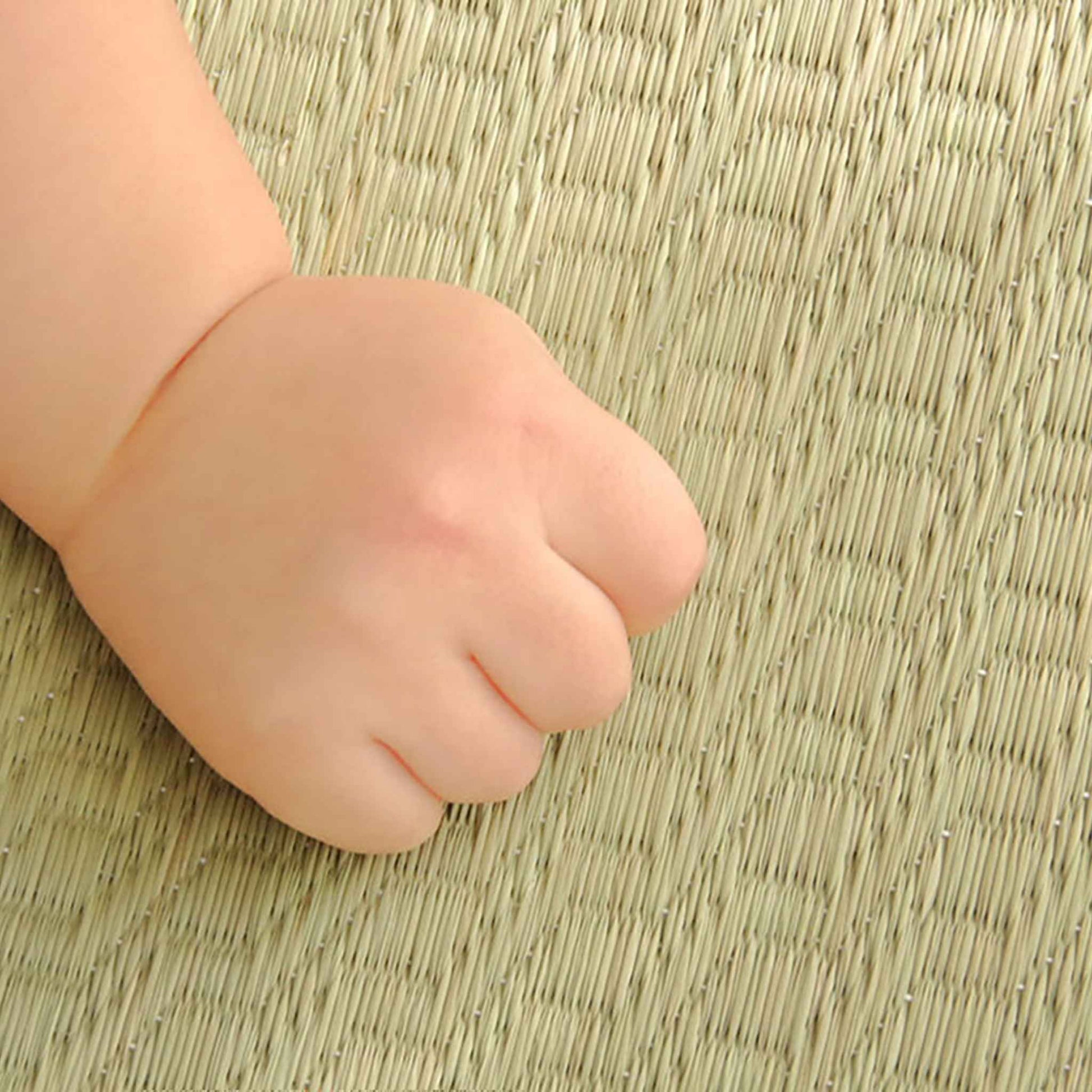 Babyhånd, der hviler på en naturlig tatamimåtte, som viser den glatte tekstur, der er sikker for følsom hud.