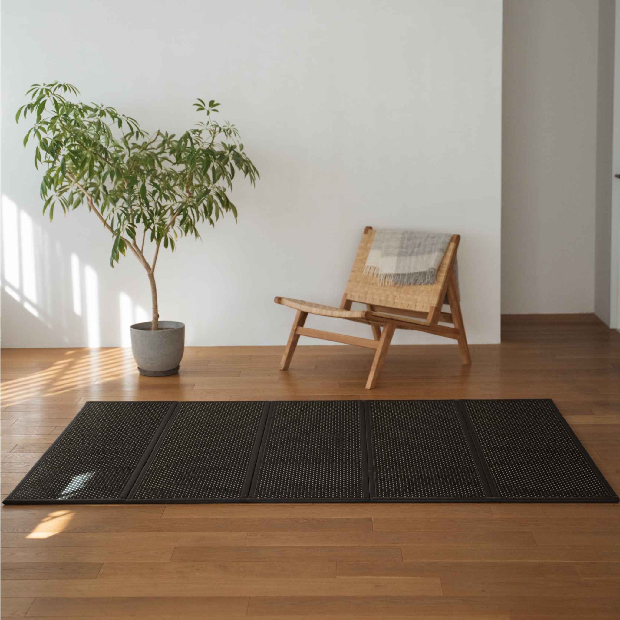 Sort tatami-måtte foldet ud på et trægulv i stuen ved siden af en stol, der fungerer som et moderne zen-område tæppe.