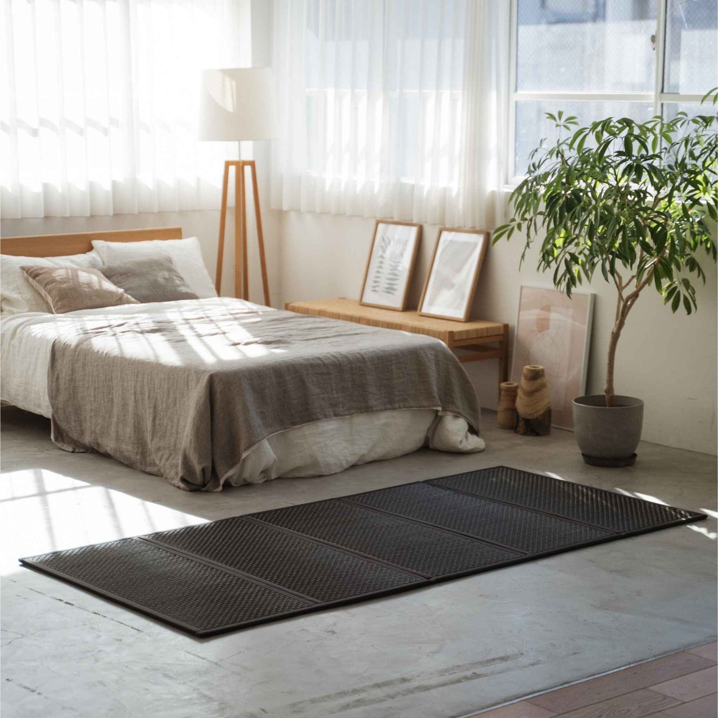 Enkel sort tatami-måtte placeret på et betongulv i et solbeskinnet rum med en minimalistisk japansk indretningsstil.