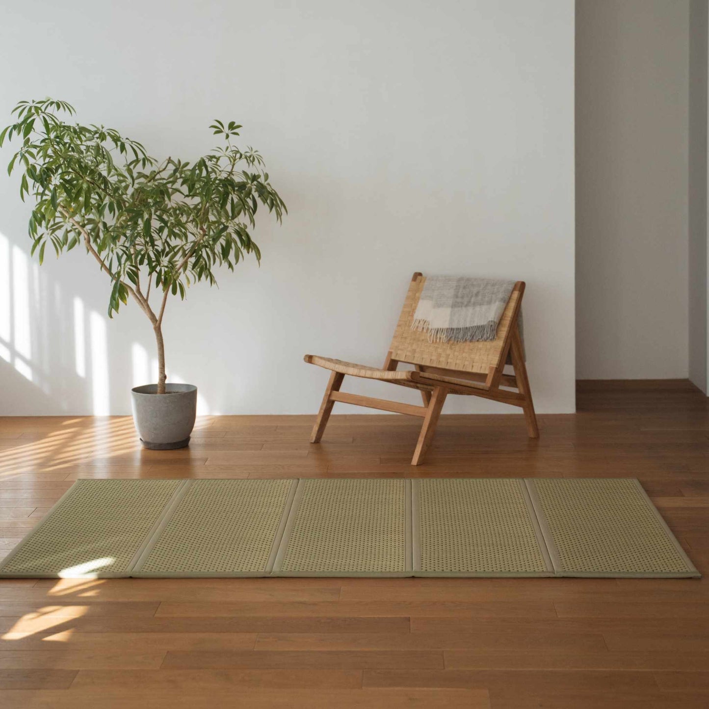 Grøn dobbelt tatami-måtte placeret på et trægulv ved siden af en stol og en plante til minimalistisk japansk indretning.