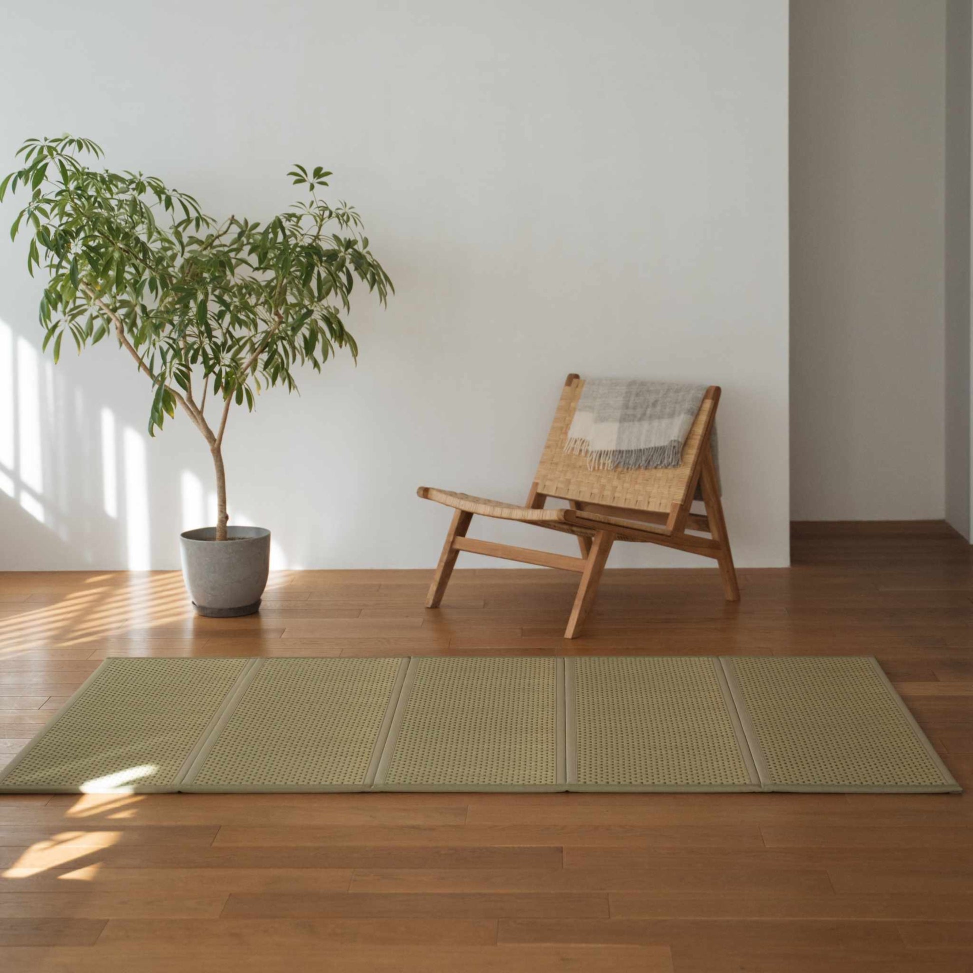Grøn dobbelt tatami-måtte placeret på et trægulv ved siden af en stol og en plante til minimalistisk japansk indretning.