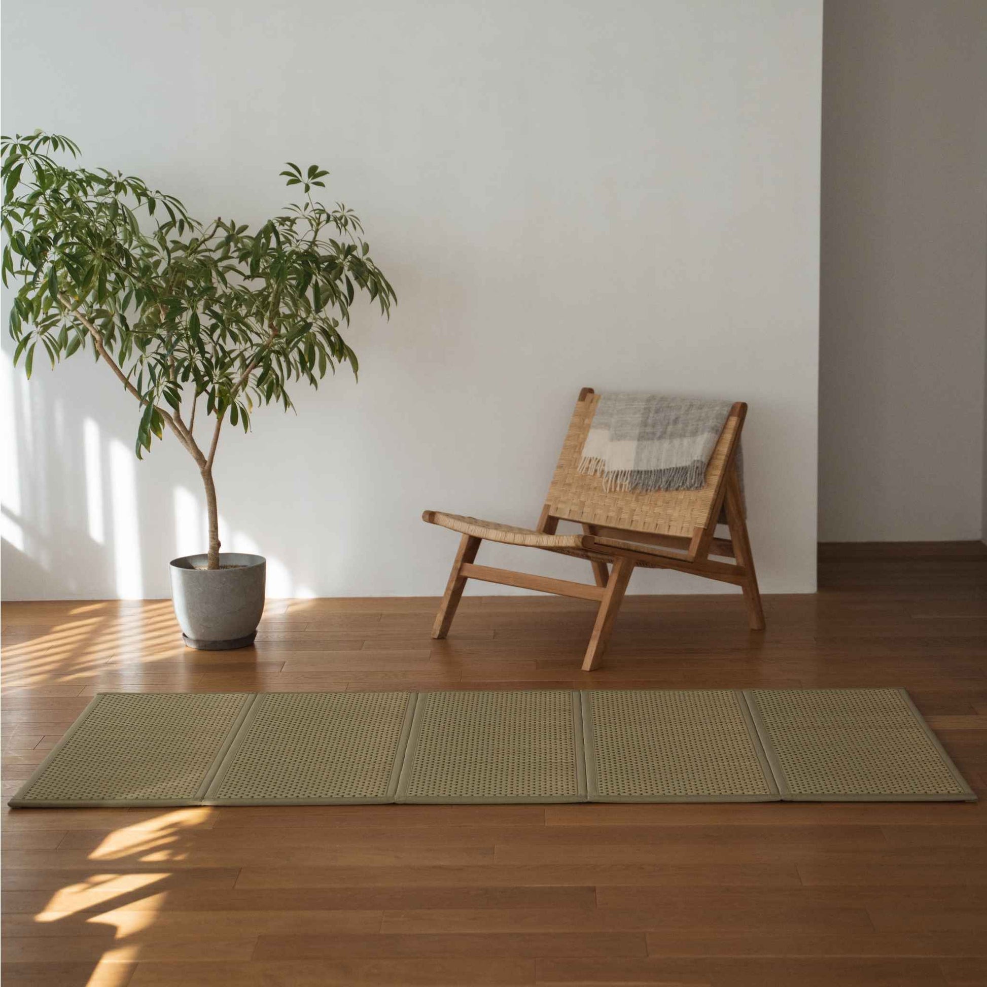 Grøn enkelt tatami-måtte placeret på et trægulv ved siden af en stol og en plante til minimalistisk japansk indretning.