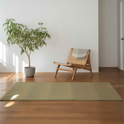 Grøn halv-dobbel tatami måtte placeret på et trægulv ved siden af en stol og en plante til minimalistisk japansk indretning.