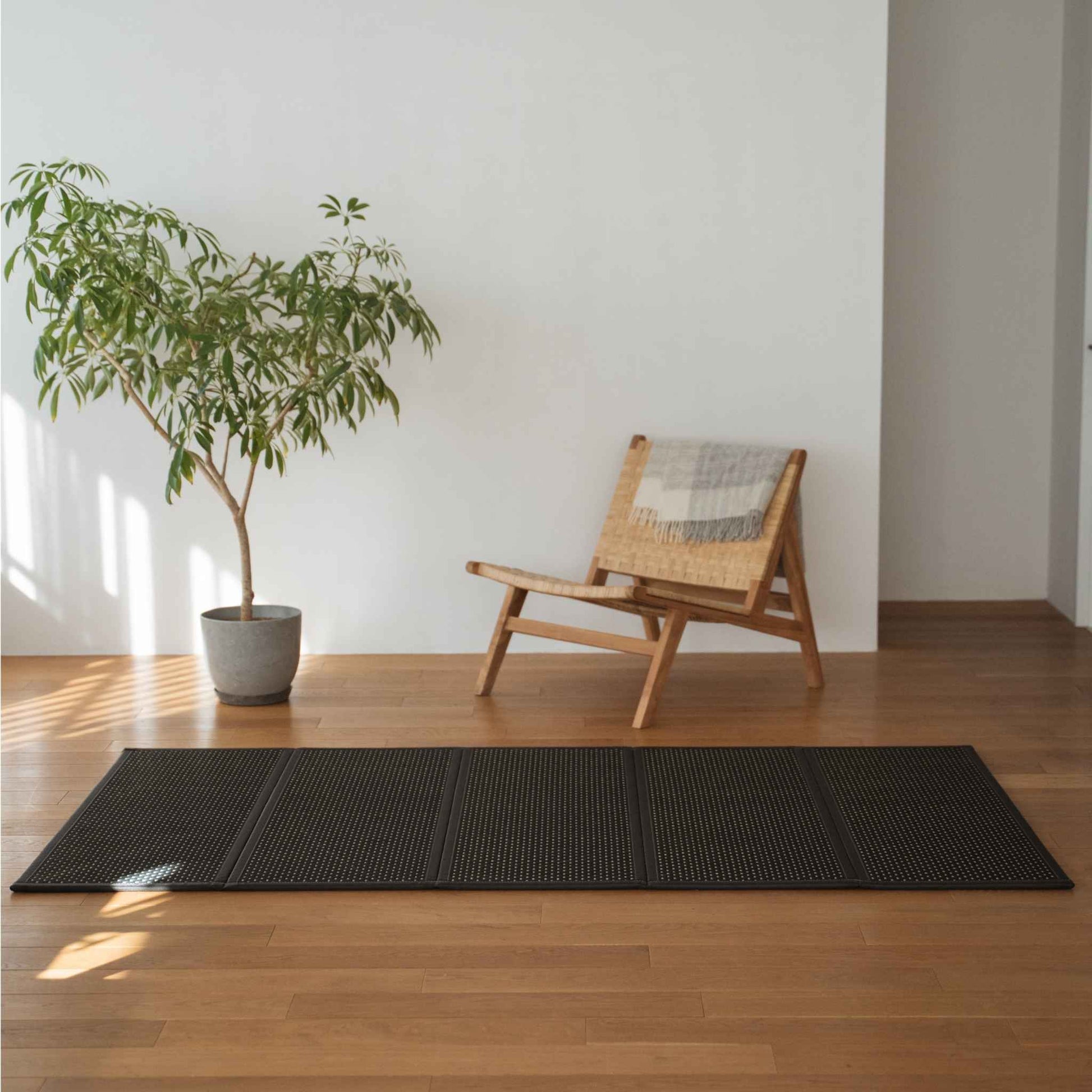 Sort tatami-måtte foldet ud på et trægulv i stuen ved siden af en stol, der fungerer som et moderne zen-område tæppe.