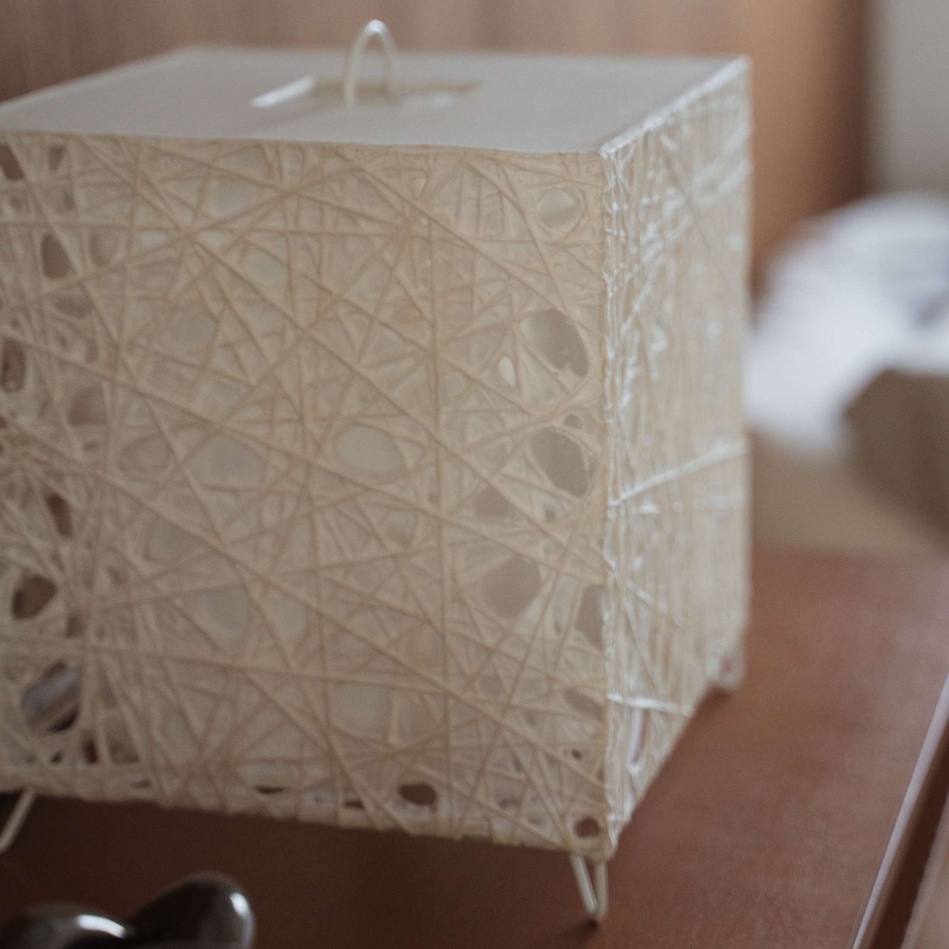 Gros plan sur la texture du papier washi blanc Melook avec des motifs de fibres complexes semblables à des toiles d'araignées sur la lampe cube.