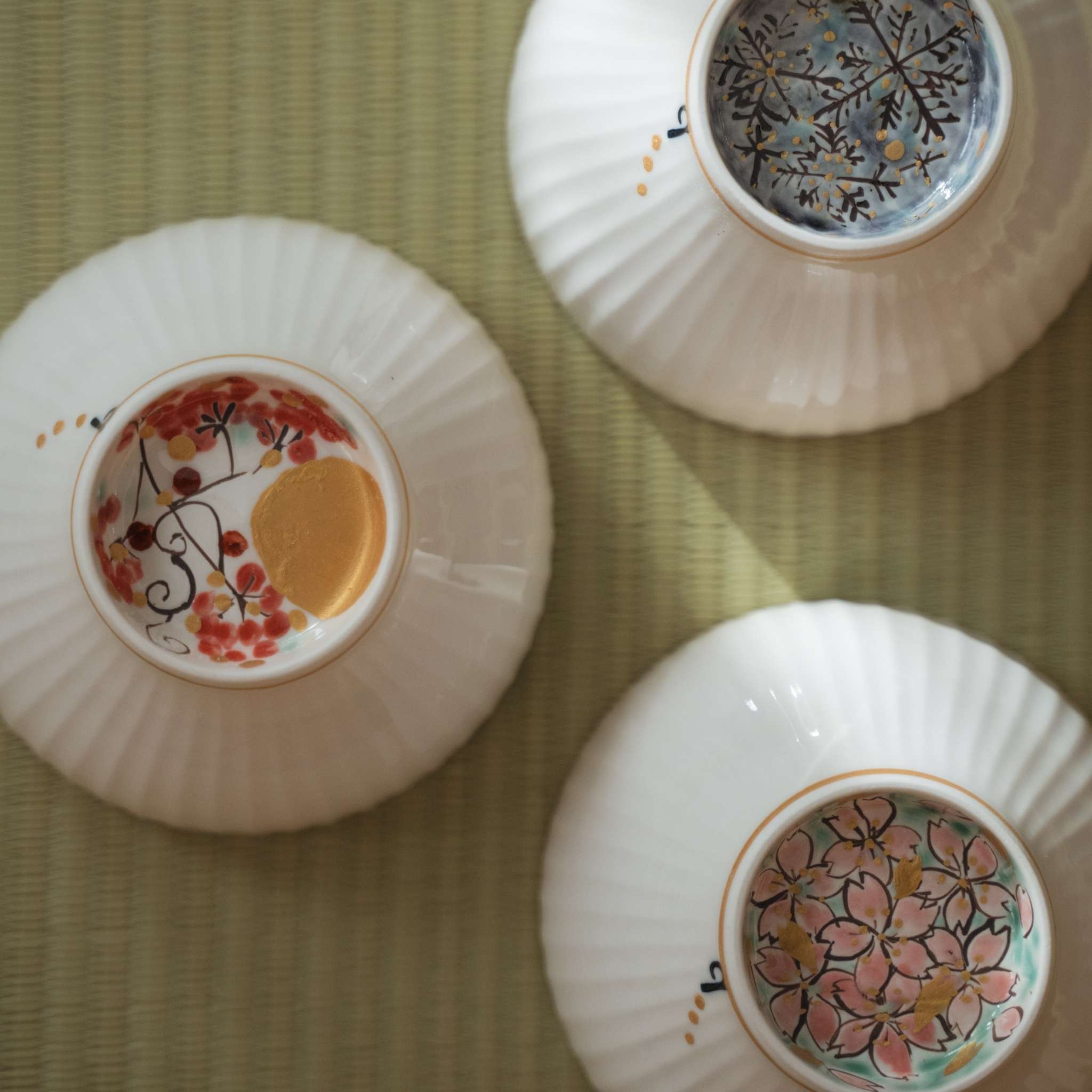 Tre japanske matcha-skåle på hovedet på en tatamimåtte med måne-, sne- og blomsterdesign på bunden.