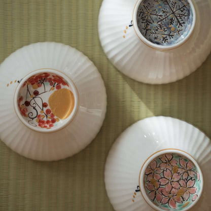 Tre japanske matcha-skåle på hovedet på en tatamimåtte med måne-, sne- og blomsterdesign på bunden.
