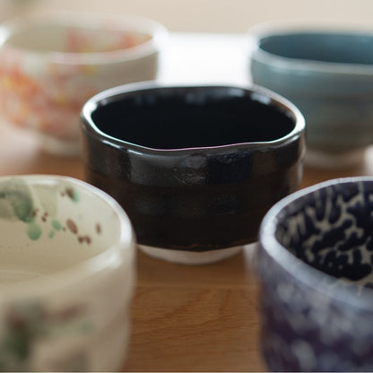 Fem forskellige japanske matcha chawan-skåle fra Mino-keramik, med en central mørk sort skål og andre med farverige glasurer og mønstre, ideel til teceremonier.