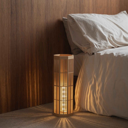 "Lampadaire japonais en bois « SAN » Grand, placé à côté d'un lit, diffusant une lumière d'ambiance chaleureuse pour une nuit paisible."