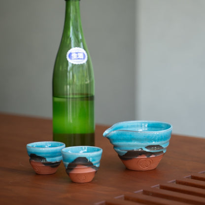 Turkisblå japansk sake-sæt (sake-karaffel, to kopper) på et træbord med en flaske, klar til en elegant middag.