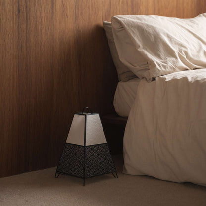 Onverlichte Japanse staande lamp KURA Klein met Seigaiha-patroon, geplaatst naast een bed in een slaapkamer in Japandi-stijl.