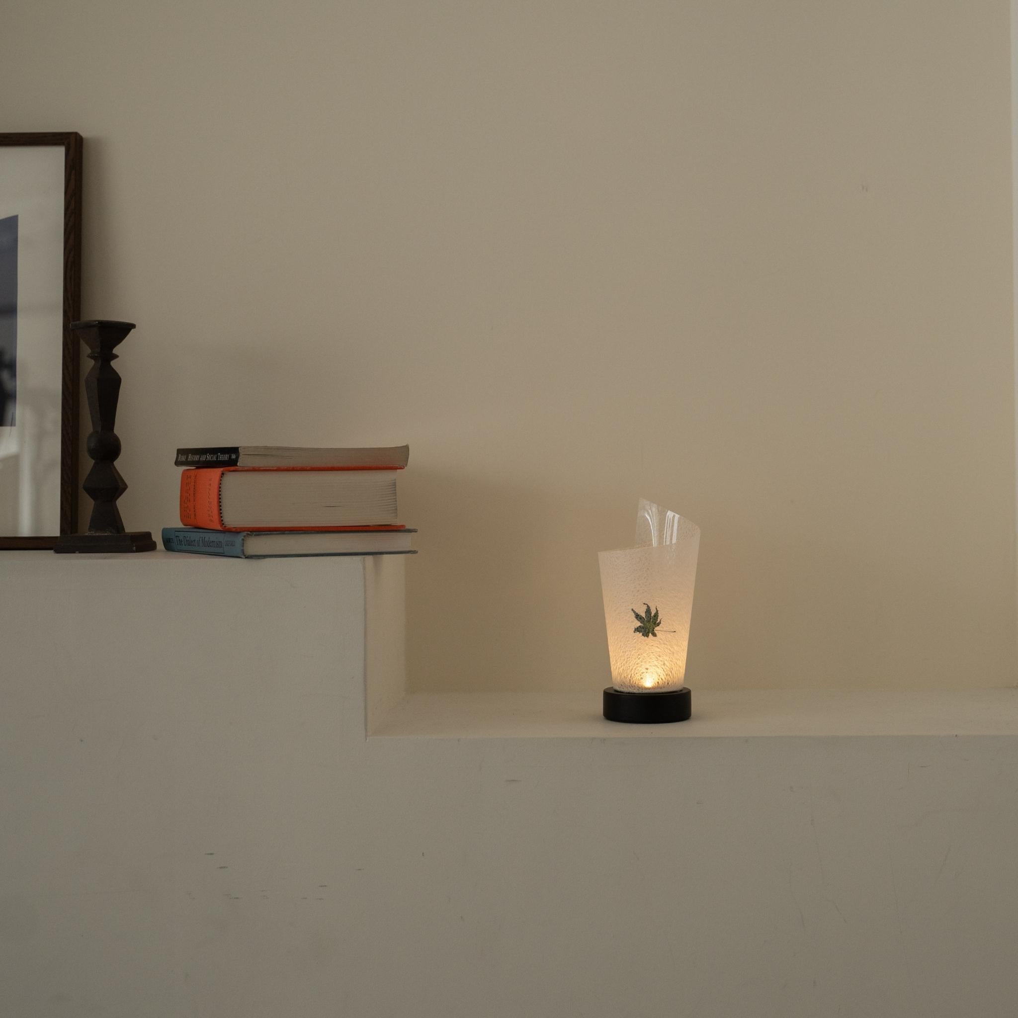 "Lampe de table japonaise en papier « Maki » avec feuille d'érable Momiji, éclairant chaleureusement comme une lampe d'ambiance sur une console blanche dans un salon Japandi."