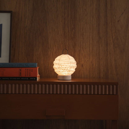Lit round Japanese paper table lamp "Yuhi" Sakura providing warm light on a mid-century modern wooden console in a living room.