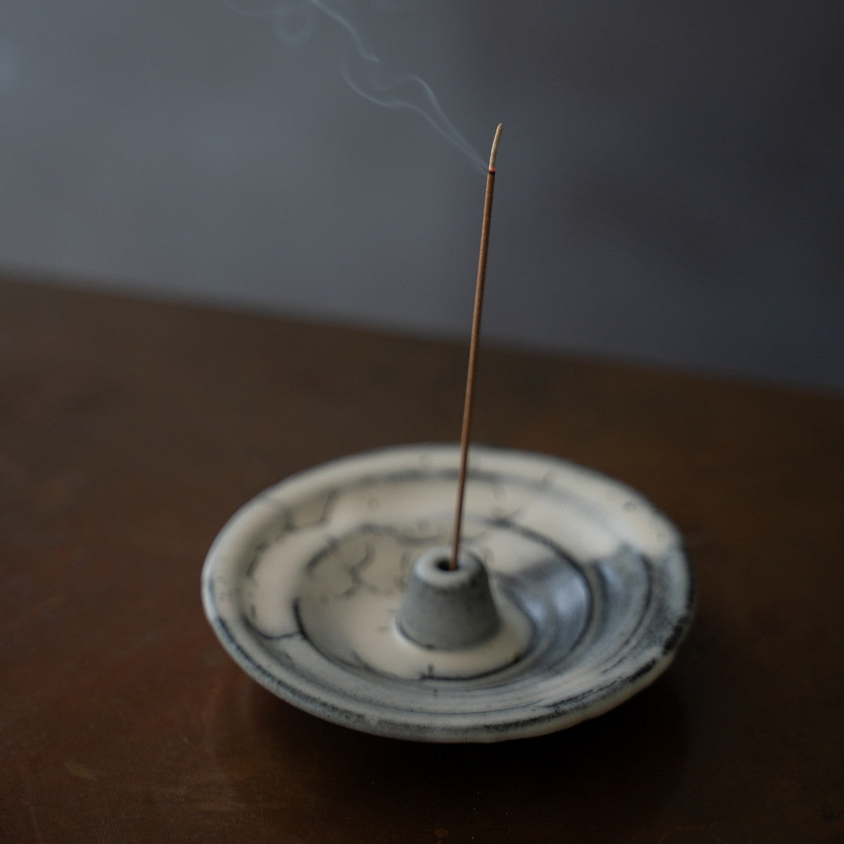 White and black ceramic Japanese incense burner on a dark surface with rising smoke, adding elegant wabi-sabi to a living space.