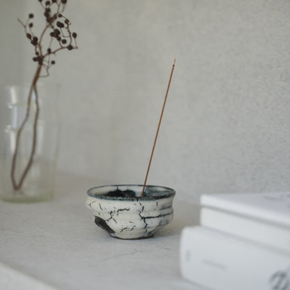 White and black deep bowl Japanese incense burner with gold and black glazes on a bright shelf, adding wabi-sabi to a Japandi living room.
