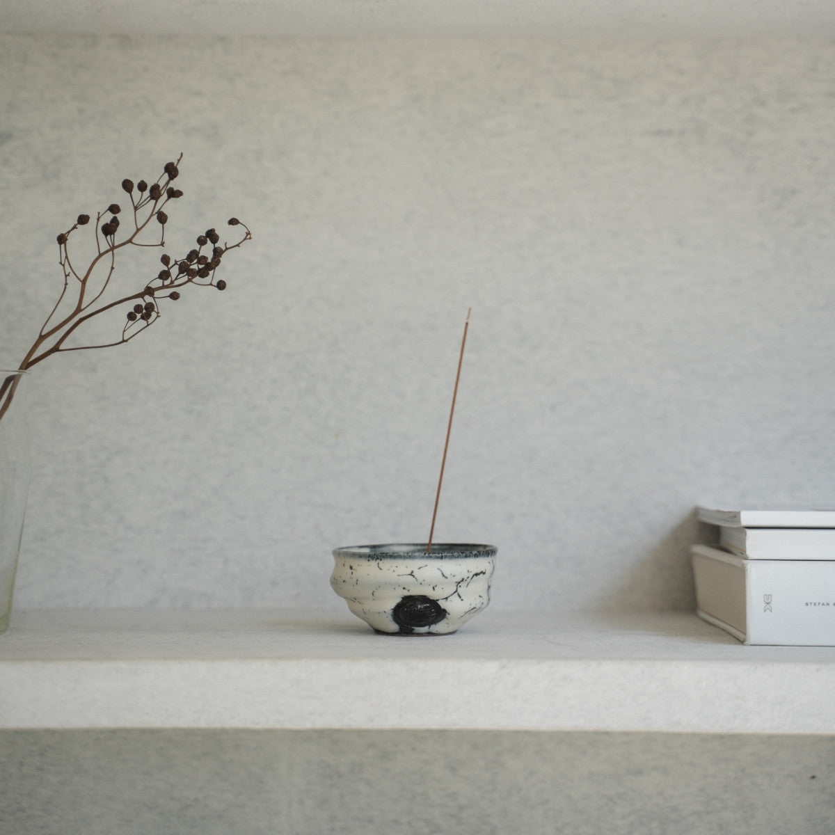 White and black Japanese incense burner on a light shelf with books, setting a serene mood for a morning yoga routine.