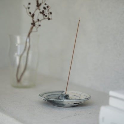 White and grey Japanese incense holder with a lit stick on a light tabletop, creating serenity for a morning meditation.