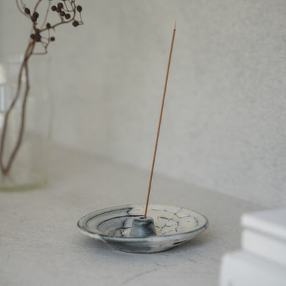 White and grey Japanese incense holder with a lit stick on a light tabletop, creating serenity for a morning meditation.