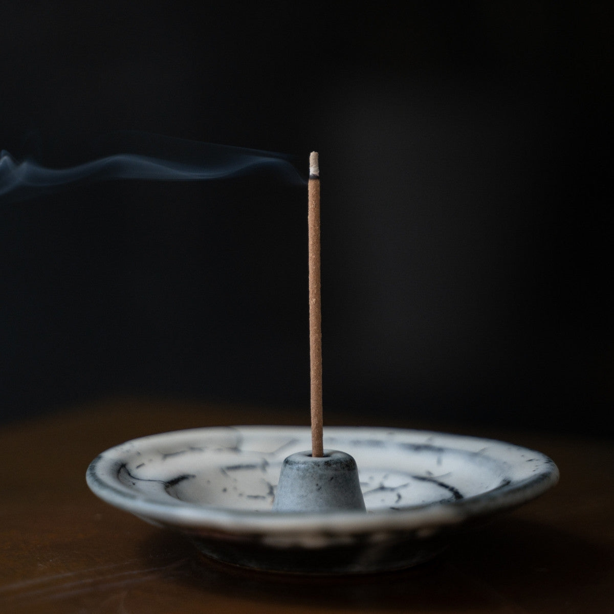 White and grey Japanese incense holder on a wooden table with drifting smoke, creating serenity for mindful meditation.