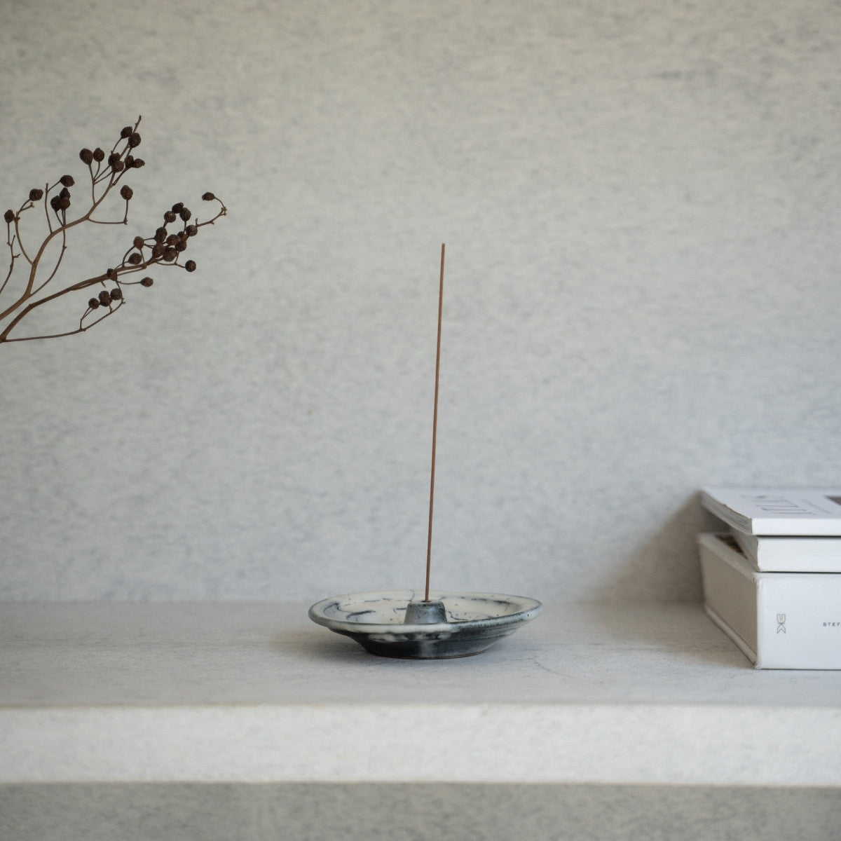 White ceramic Japanese incense burner on a minimalist shelf with books, adding a wabi-sabi touch to a modern living room.
