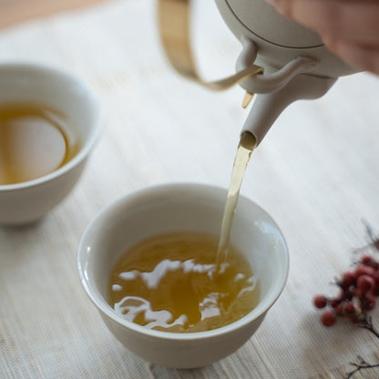Remplissage de tasses à thé japonaises blanches avec une théière kyusu sur une table lumineuse pour des amateurs de thé profitant d'une pause d'après-midi apaisante.
