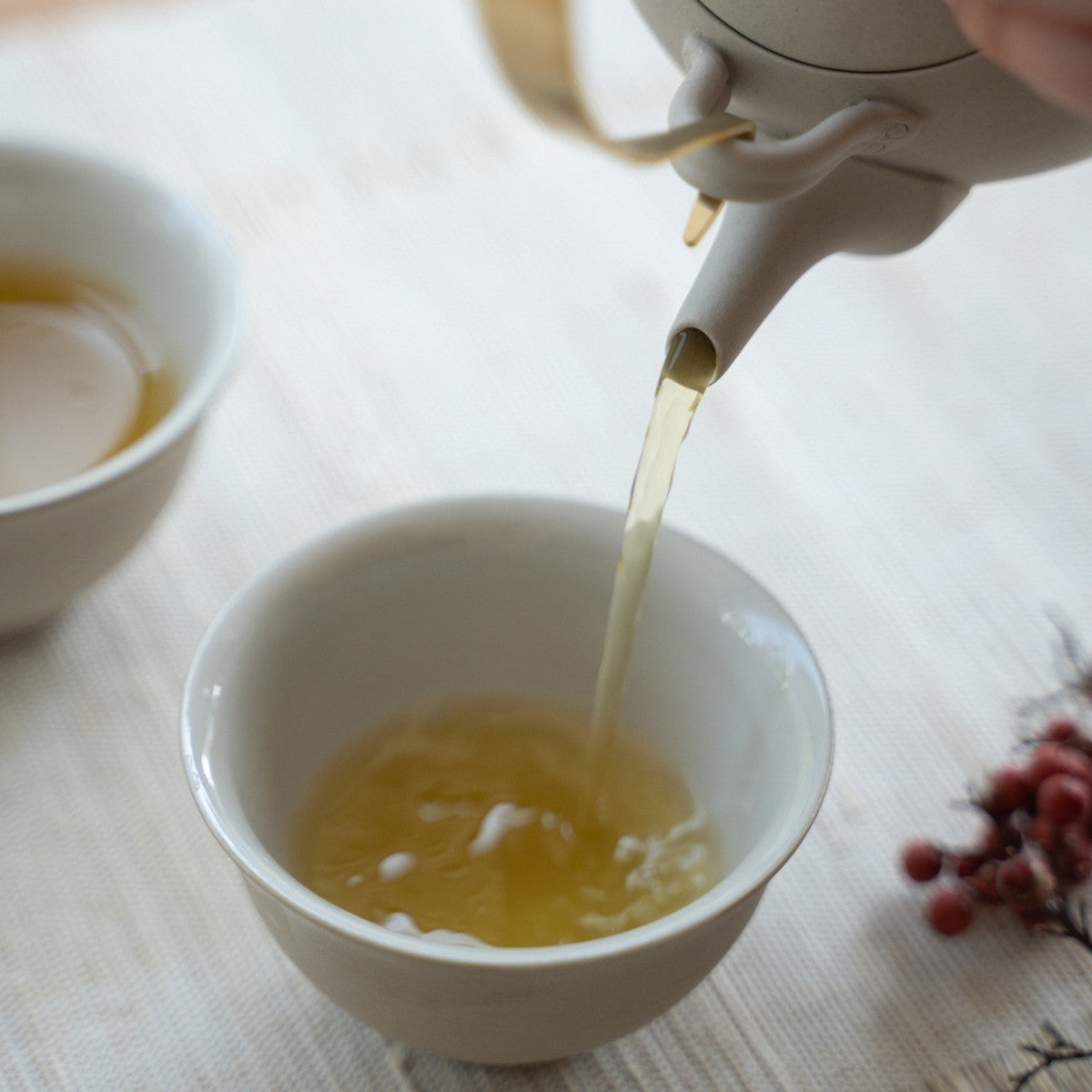 Service à thé japonais blanc "Donguri" versant une infusion fraîche dans un espace ensoleillé pour les amateurs de thé savourant un moment de bien-être aromatique.