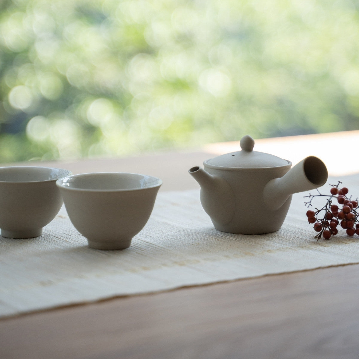 White kyusu teapot "Fuyo" and Japanese tea cups on a sunlit table for wellness seekers enjoying a mindful conversation.