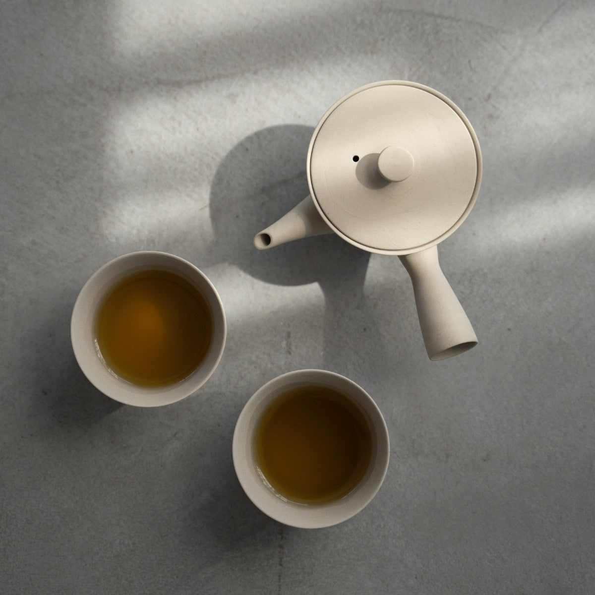 White Japanese tea set "Sencha" with brewed tea on a concrete surface for minimalists enjoying a calm wellness ritual.