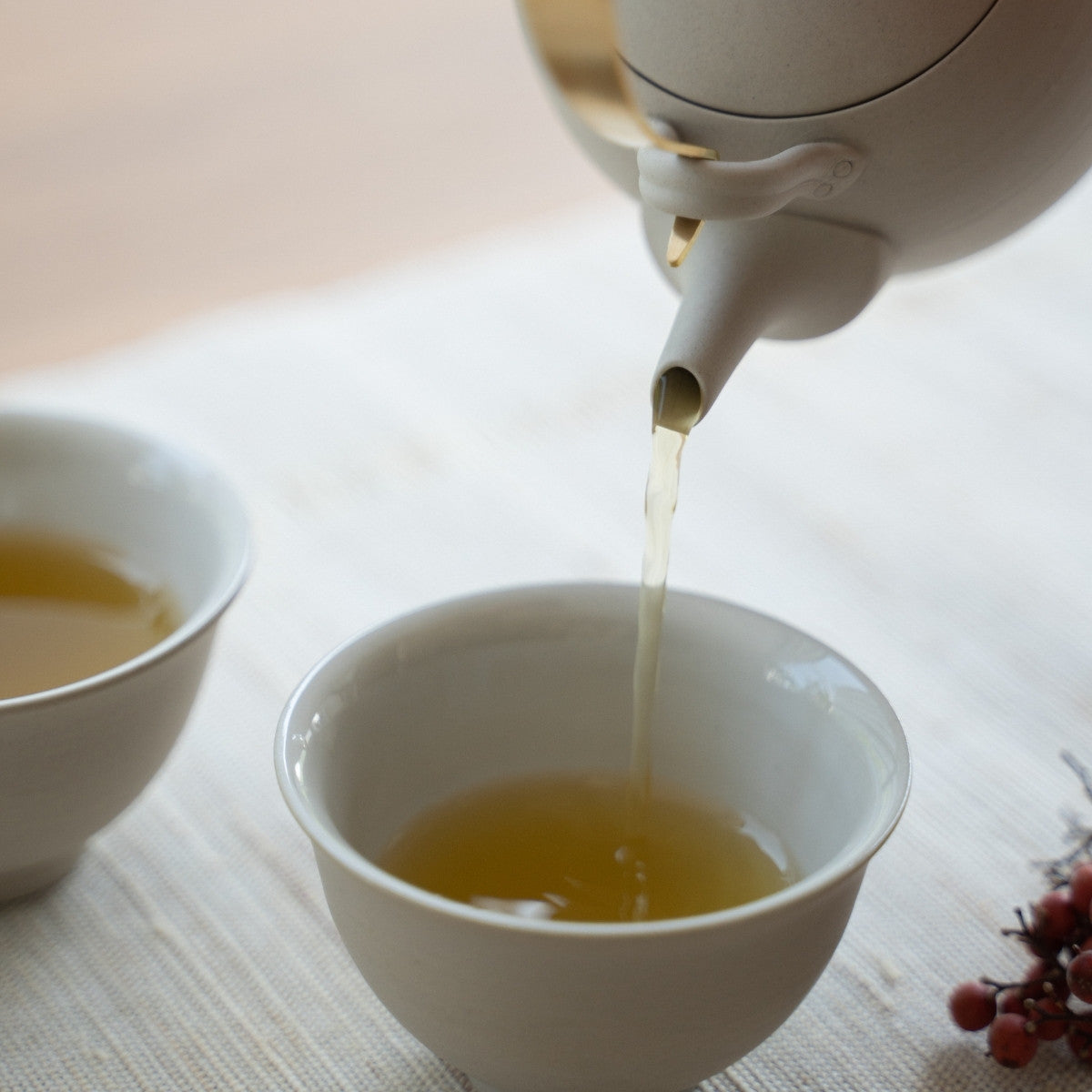 Pouring green tea from a white Japanese teapot "Donguri" into a cup on a linen mat for guests experiencing elegant hospitality.
