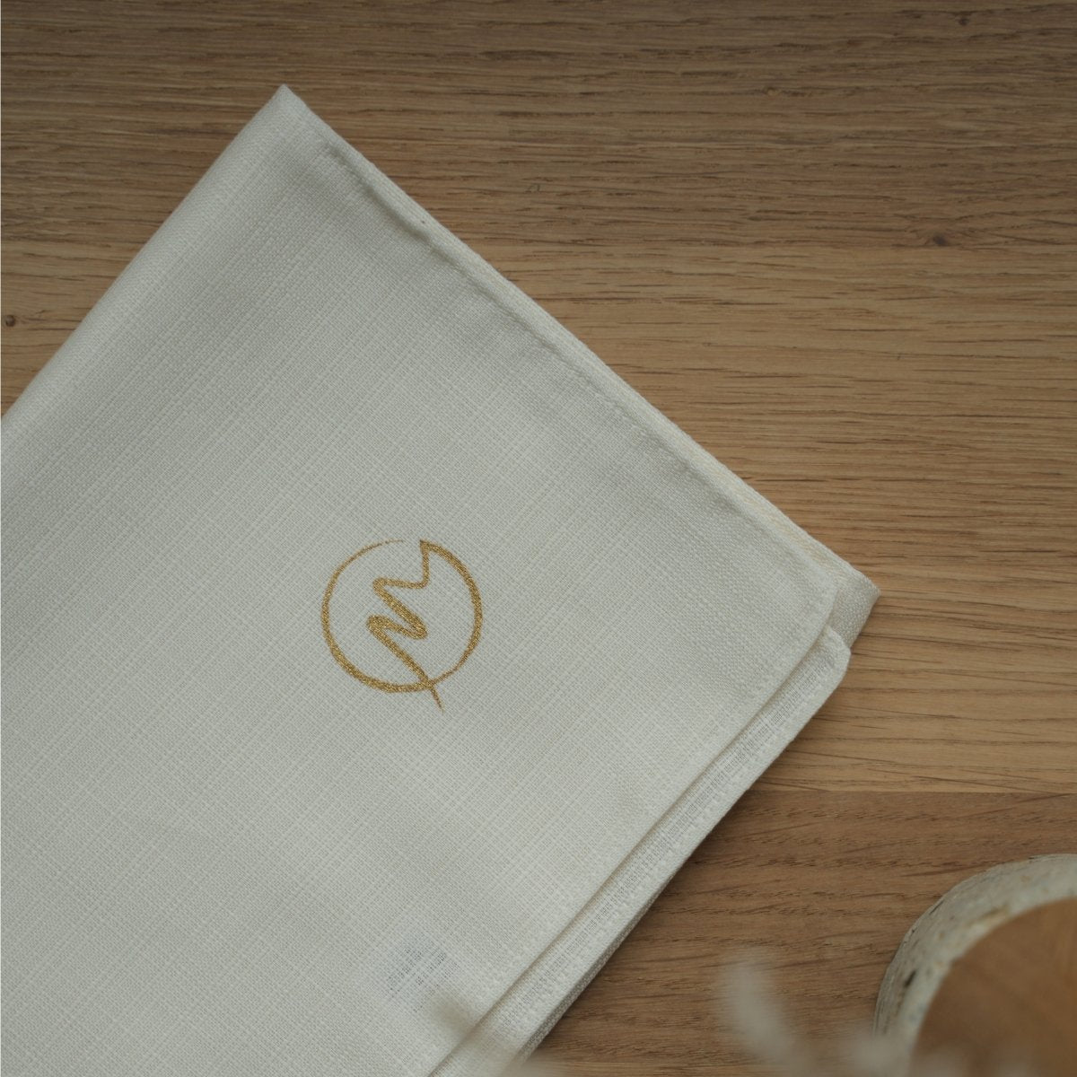 Folded white fabric gift wrap with a gold logo on a wooden table, preparing an elegant Japanese gift.