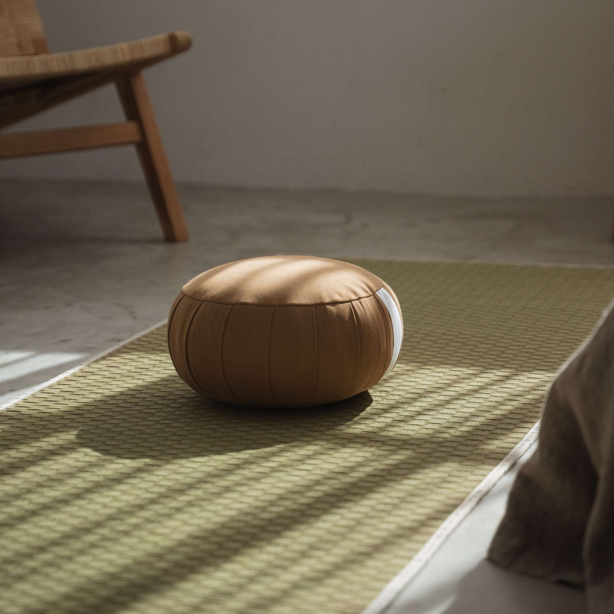 Autentisk karamelbrun zafu meditationspude, der hviler på en traditionel tatami-måtte med naturligt vindueslys.