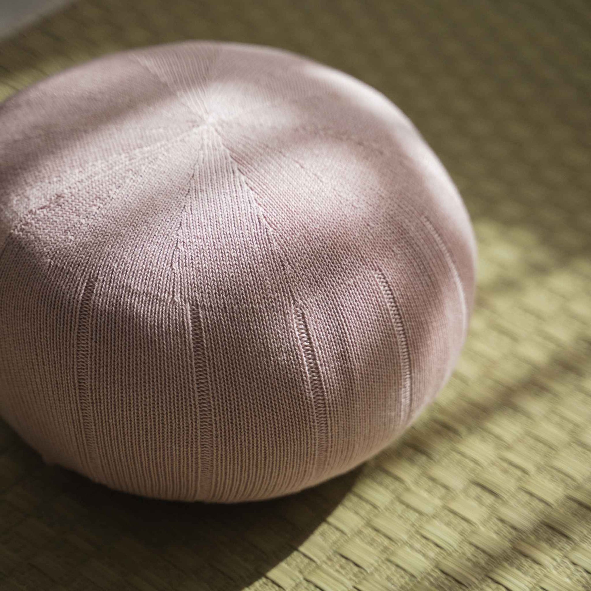 Gros plan d'un coussin de méditation zafu rose brumeux montrant la texture tricotée en coton biologique sur un tapis tatami.