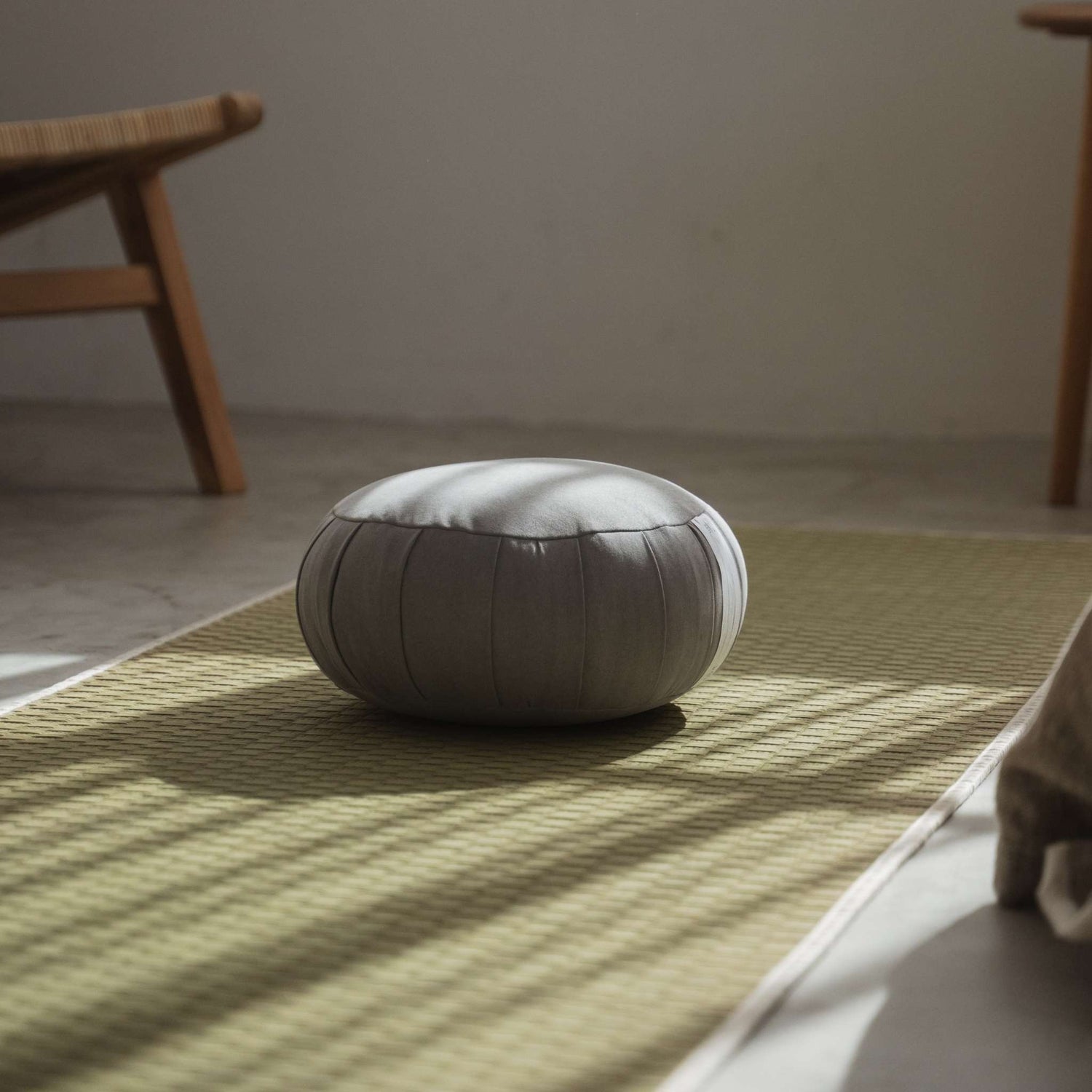 Zilver grijze zafu meditatiekussen geplaatst op een groene tatamimat in een minimalistische zenruimte voor mindfulness.