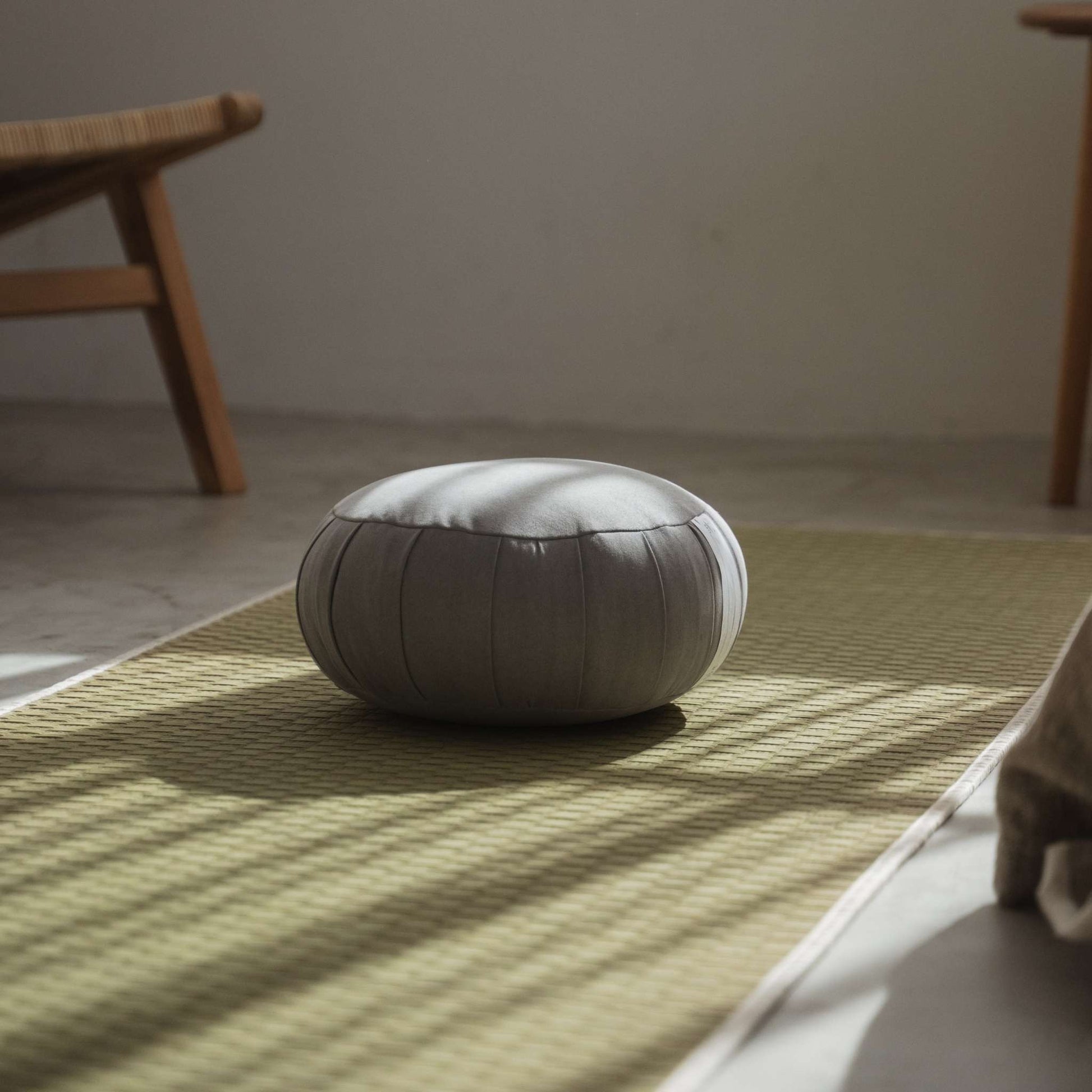 Zilver grijze zafu meditatiekussen geplaatst op een groene tatamimat in een minimalistische zenruimte voor mindfulness.