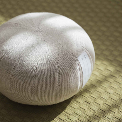 Nahaufnahme eines weißen, grauen Zafu-Meditationskissens, das die organische Baumwollstricktextur auf einer Tatami-Matte zeigt.