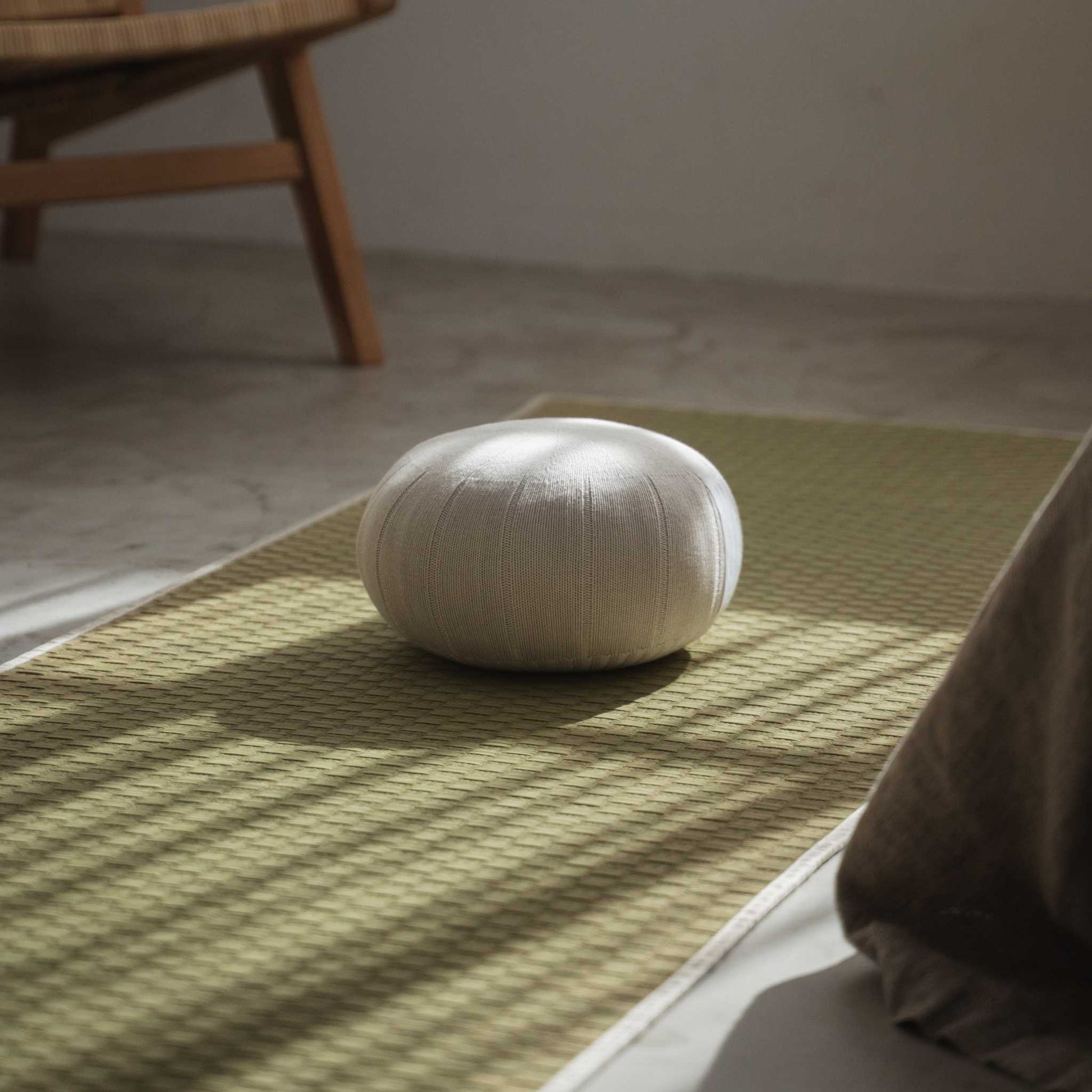 Weißgraues Zafu-Meditationskissen auf einer grünen Tatami-Matte in einem friedlichen, sonnendurchfluteten Zen-Raum.
