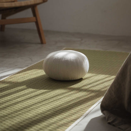 Weißgraues Zafu-Meditationskissen auf einer grünen Tatami-Matte in einem friedlichen, sonnendurchfluteten Zen-Raum.