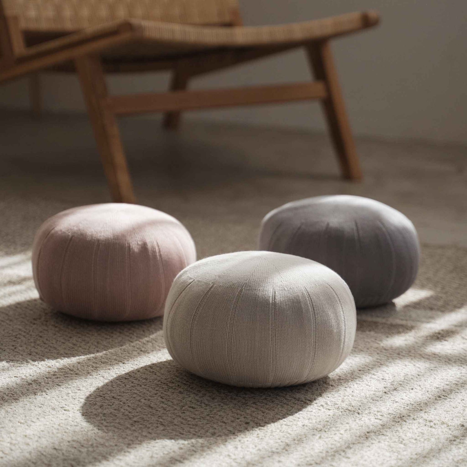 Trio af runde japanske zafu meditationspuder siddende på et tæppe i et solbeskinnet rum nær en træstol.